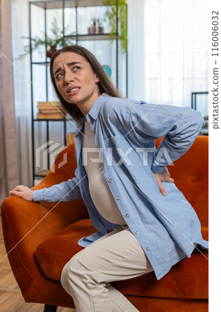 Upset ill young pregnant woman feeling sick suffering from lower back pain sitting on home sofa Upset ill young pregnant woman feeling sick suffering from lower back pain sitting on home sofa 116006032