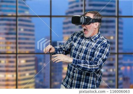 Portrait of an elder man in vr headset with his mouth open. Checkered window background with night cityscape view. 116006063
