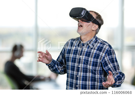 Excited elder man wearing vr headset with his mouth open. Indoor office enviroment background. 116006068