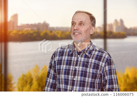 Portrait of happy cheerful caucasian man is looking up standing in office. River scape background. 116006075