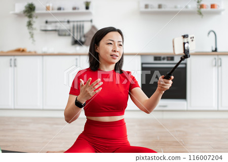 Woman recording online blog for studying on phone in kitchen 116007204