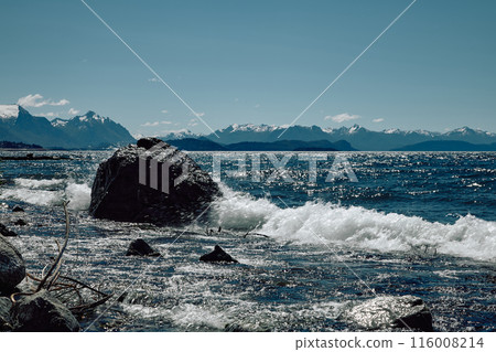 The surf of a turquoise lake washes over a huge black boulder. The surf of a turquoise lake washes over a huge black boulder. 116008214