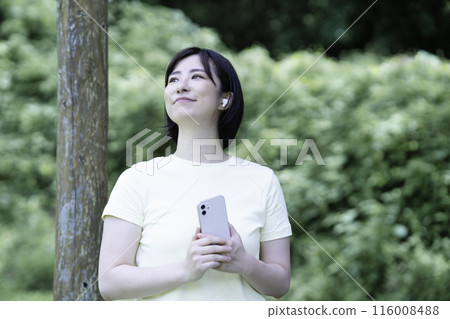 A woman relaxing listening to music among the fresh greenery A woman relaxing listening to music among the fresh greenery 116008488