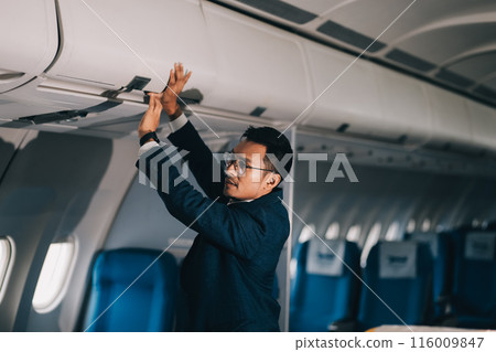 man putting luggage on the top shelf on airplane 116009847