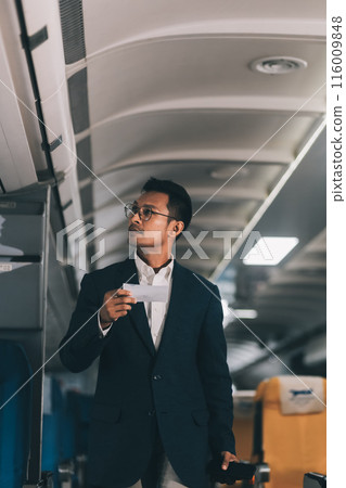 Handsome Asian male passenger takes his carry-on luggage out of the overhead locker after landing at his destination. transportation concept 116009848