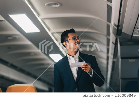 Handsome Asian male passenger takes his carry-on luggage out of the overhead locker after landing at his destination. transportation concept 116009849
