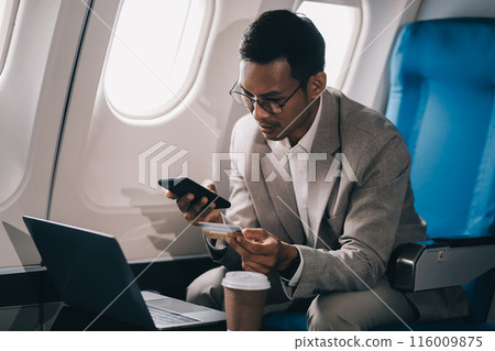 Businessman holding credit card and looking at camera near laptop in private jet Businessman holding credit card and looking at camera near laptop in private jet 116009875