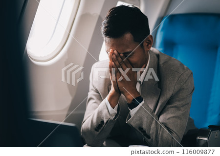 Stressed and professional Asian businessman in a business class, having a serious phone call with someone during the flight to a business meeting. Stressed and professional Asian businessman in a business class, having a serious phone call with someone during the flight to a business meeting. 116009877