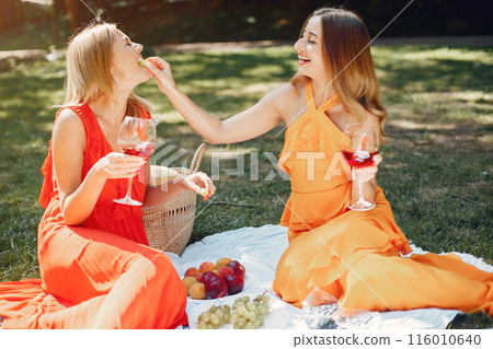 Beautiful girl in a red dress. Women sitting in a summer park. 116010640