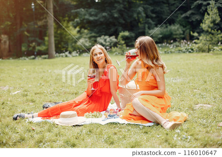 Beautiful girl in a red dress. Women sitting in a summer park. 116010647