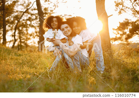 Photo of caucasian mother and two her african american daughters embracing together outdoors. Girls has black curly hair. Mother and daughers wearing white t-shirts. Photo of caucasian mother and two her african american daughters embracing together outdoors. Girls has black curly hair. Mother and daughers wearing white t-shirts. 116010774