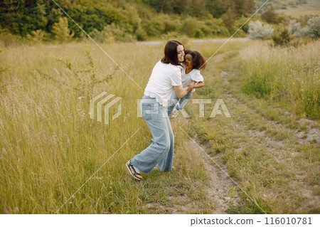 Photo of caucasian mother and her african american daughter together. Girl has black curly hair. Mother and daugher wearing white t-shirts. Photo of caucasian mother and her african american daughter together. Girl has black curly hair. Mother and daugher wearing white t-shirts. 116010781