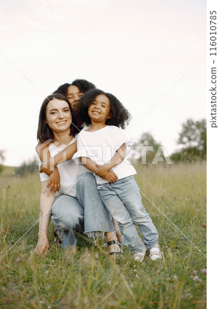 Photo of caucasian mother and two her african american daughters embracing together outdoors. Girl shas black curly hair. Mother and daughers wearing white t-shirts. 116010785