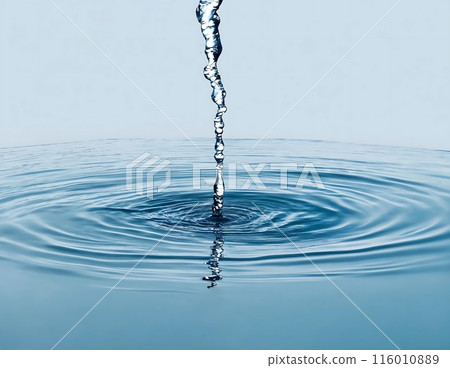 Close-up shot of water pouring into a still pool of water, creating a perfect circular ripple effect. The stream of water is thin and transparent, while the pool is a light blue.	 116010889