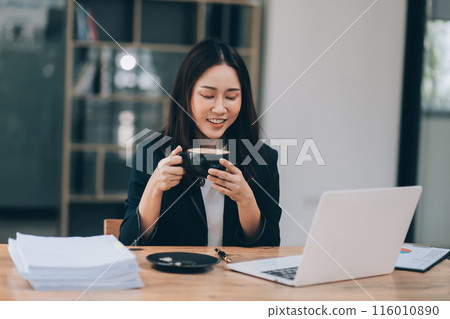 Beautiful young Asian businesswoman smiling holding a coffee mug and laptop working at the office. 116010890