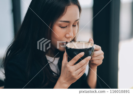 Beautiful young Asian businesswoman smiling holding a coffee mug and laptop working at the office. 116010891