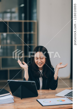 Pretty young Asian businesswoman working on laptop and taking notes In office. 116010893