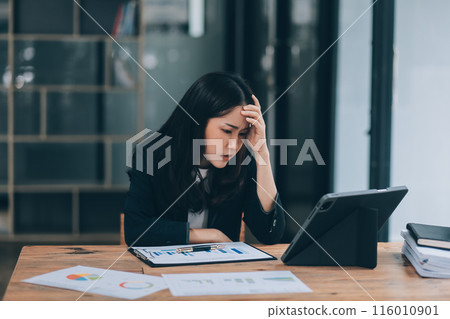 Young sad businesswoman is sitting at table, covering his face On desk is laptop, tablet computer, Stress. Serious woman concentrating on his paper work. 116010901