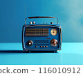 Vintage blue radio with a chrome antenna, knobs, and trim is sitting on a blue surface. The radio has a classic design and is likely from the mid-20th century. 116010912