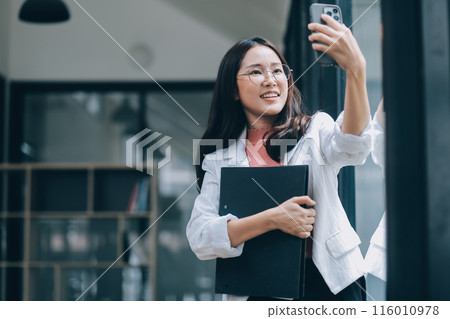 Portrait of a happy Asian businesswoman using mobile phone indoor, Asian businesswoman working in modern office. 116010978