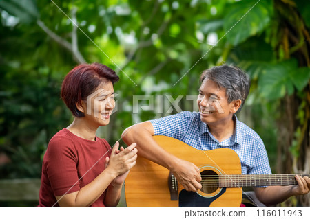 Middle aged  couple playing guitar while relax sitting on bench in backyard. 116011943