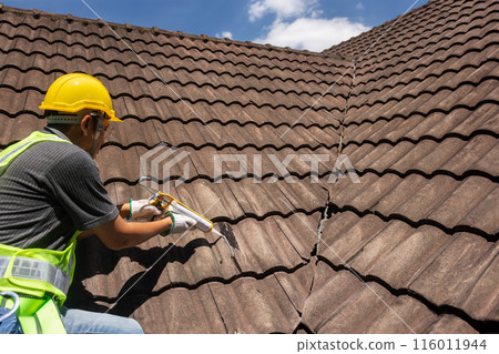 Worker man using silicone sealant adhesive to fix crack of the old tile roof. Worker man using silicone sealant adhesive to fix crack of the old tile roof. 116011944