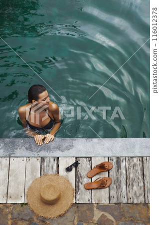 Woman Relaxing in Pool with Sun Hat and Sandals on Deck 116012378
