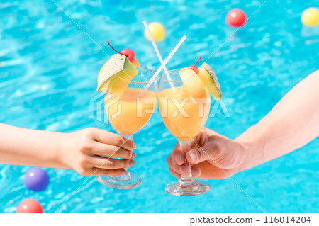 Couple toasting with tropical drinks by the pool at a vacation resort hotel 116014204