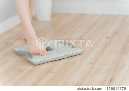 The feet of a woman standing on a weight scale, body composition scale, and body fat scale 116014876