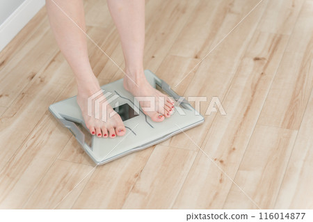The feet of a woman standing on a weight scale, body composition scale, and body fat scale 116014877
