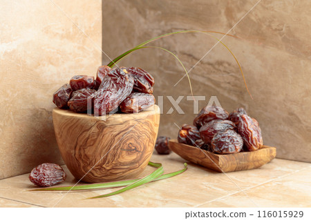 Dates fruit in a wooden dish on a beige ceramic table. Dates fruit in a wooden dish on a beige ceramic table. 116015929