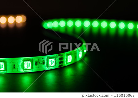 Bobbin with roll of glowing LED strip lighting placed on table, green and warm white color Bobbin with roll of glowing LED strip lighting placed on table, green and warm white color 116016062