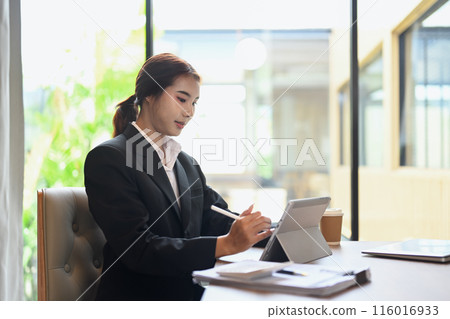 Portrait young female professional wearing formal suit working on digital tablet in modern office Portrait young female professional wearing formal suit working on digital tablet in modern office 116016933