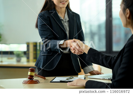 Female lawyer shaking hand with client standing at the desk with contract document and judge's gavel 116016972