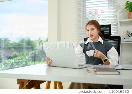 Asian woman freelancer drinking coffee and working with laptop at office Asian woman freelancer drinking coffee and working with laptop at office 116016980