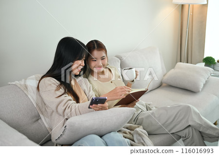 Happy Asian lesbian couple relaxing on couch and reading book together. LGBTQ people lifestyle concept 116016993