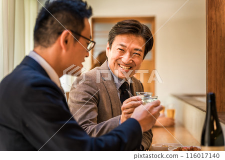 A businessman man who enjoys drinking alcohol with his subordinates at the counter of an izakaya bar 116017140