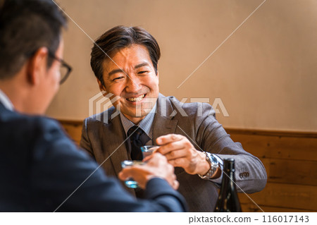 一位中年亞洲商人在酒吧與下屬和同事喝酒。 一位中年亞洲商人在酒吧與下屬和同事喝酒。 116017143