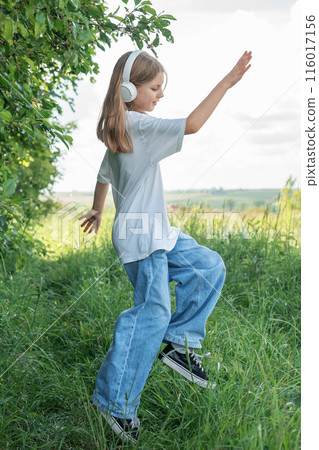 A child with headphones listening to music and dancing in the park.. A child with headphones listening to music and dancing in the park.. 116017156
