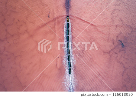 Aerial view of an old train rides on the railway laid in the water through the salt lake. Salt mining in Lake Burlin. Altai. Bursol. 116018050