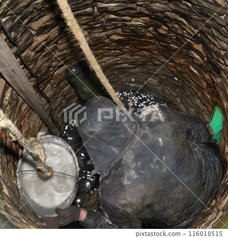 A man disinfects stones inside a well after cleaning the bottom. A man disinfects stones inside a well after cleaning the bottom. 116018515