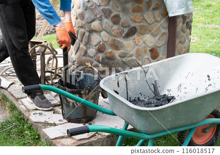 A man pours mud from a bucket into a wheelbarrow from the bottom of a well. 116018517