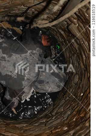 A worker stands at the bottom of a well with a bucket into which water is collected. 116018519