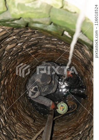 A man in the middle of a well cleans the bottom of dirt and accumulated silt. A man in the middle of a well cleans the bottom of dirt and accumulated silt. 116018524