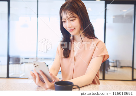 一位女士在辦公室食品儲藏室裡看著她的智慧型手機 116018691