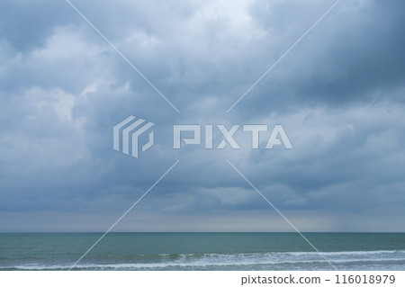 Fluffy clouds drift across a bright summer sky above a tropical beach with turquoise waves lapping at the shore 116018979