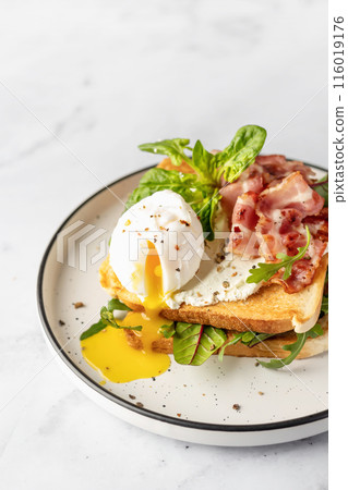 Toasts sandwich with poached egg, arugula, bacon and cream cheese on white plate marble background. Isolated, text space 116019176