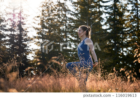Middle-aged woman trying to do difficult yoga pose. Sporty female meditating on fresh air. Meditation at dawn in coniferous forest. Middle-aged woman trying to do difficult yoga pose. Sporty female meditating on fresh air. Meditation at dawn in coniferous forest. 116019613