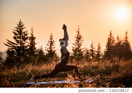 Attractive woman doing warrior one pose at dawn. Meditation in mountains at sunrise. Workout at fresh air high on hills. 116019617