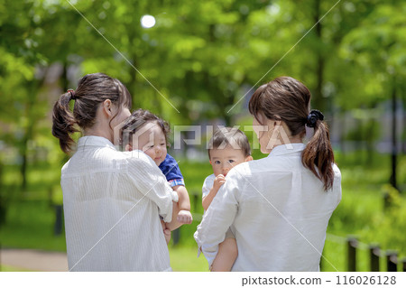 兩組家長和孩子抱著一個幼兒在公園聊天 兩組家長和孩子抱著一個幼兒在公園聊天 116026128